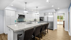 A modern kitchen with white cabinets, stainless steel appliances, a marble island, and bar stools. - Charming 3-bedroom house in lovely San Clemente with AC, Walk to the Pier! (San Clemente)