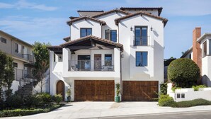 A two-story house with a wooden front door, a balcony, and a garage. - Charming 3-bedroom house in lovely San Clemente with AC, Walk to the Pier! (San Clemente)