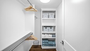 A narrow hallway with a white wall, a wooden floor, and a white shelving unit with folded towels and storage boxes. - Charming 3-bedroom house in lovely San Clemente with AC, Walk to the Pier! (San Clemente)