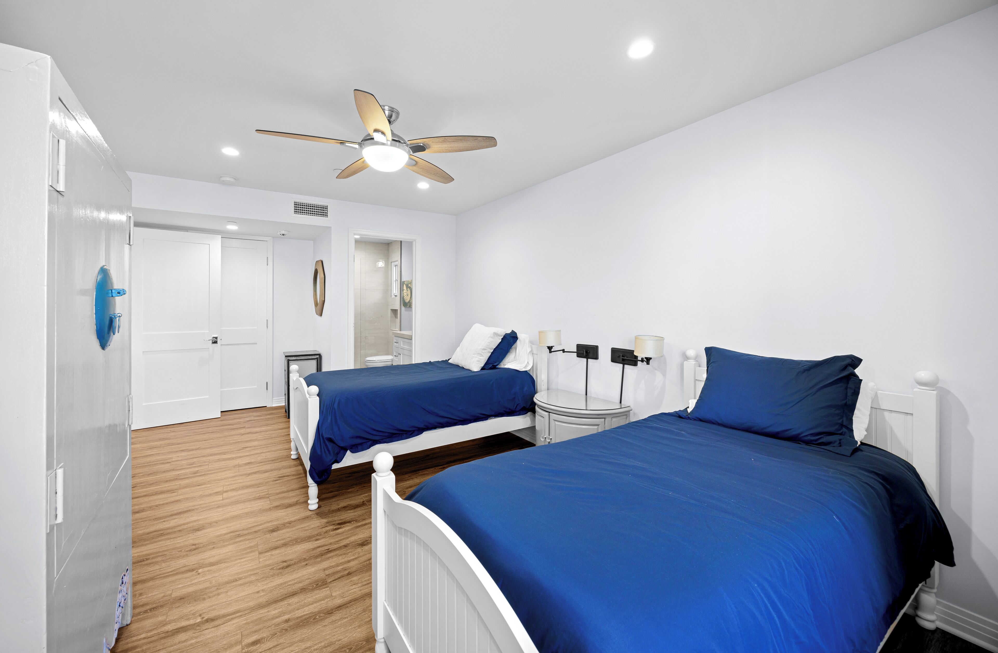 Une chambre avec deux lits, un ventilateur de plafond et une armoire blanche.