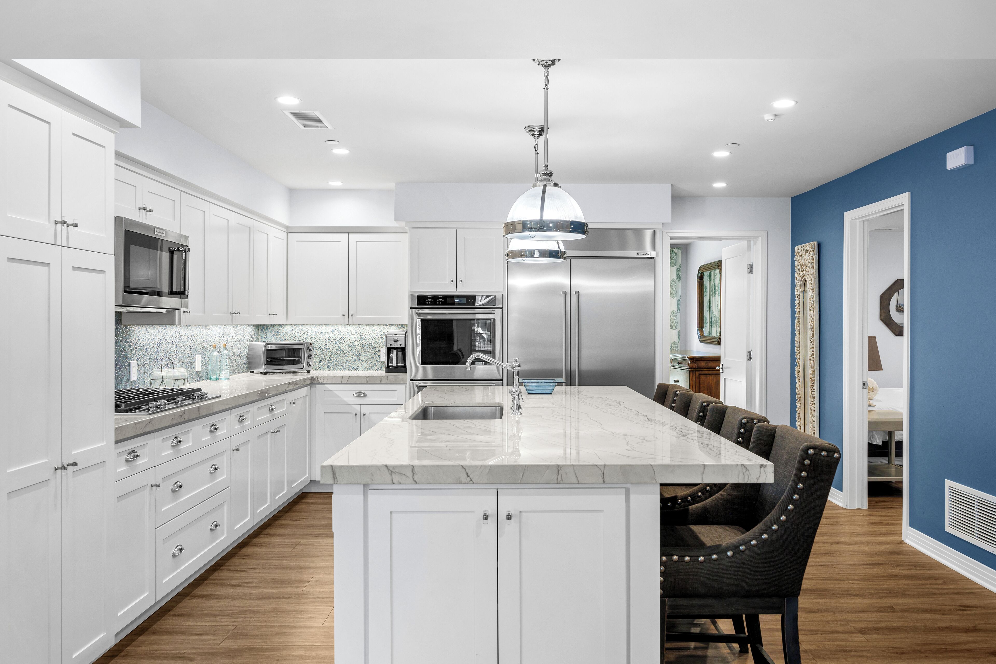 A modern kitchen with white cabinetry, stainless steel appliances, a marble island, and a dining area with a blue accent wall.