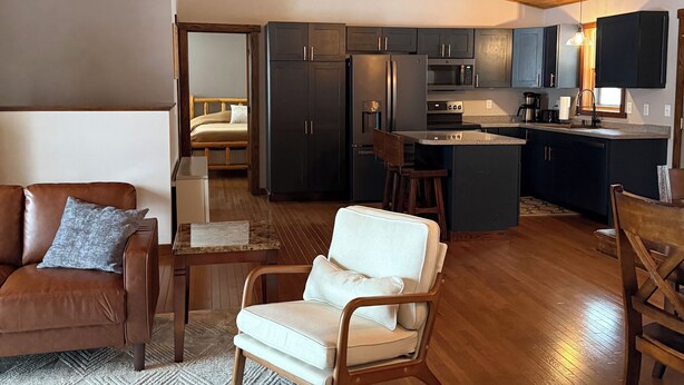 A spacious living area with a wooden ceiling, a sofa, a chair, and a kitchen area with dark cabinets and a central island. - Spacious 5BR Cabin on 6th Crow Wing Lake Near Nevis, MN (Nevis)