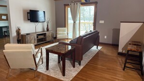 A living room with a wooden ceiling, a television mounted on the wall, a sofa, a coffee table, and a window with curtains. - Spacious 5BR Cabin on 6th Crow Wing Lake Near Nevis, MN (Nevis)