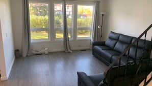 A living room with a black leather sofa, a staircase, and large windows with curtains. - Room for Rent (Calgary)