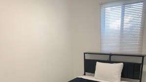 A single bed with a black metal frame and a dark blue bedspread in a room with light wooden flooring and white walls. - Room for Rent (Calgary)