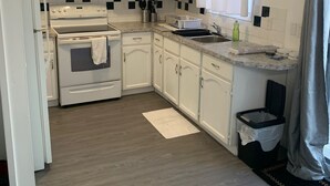 A compact kitchen with white cabinets, a stove, and a sink. - Room for Rent (Calgary)