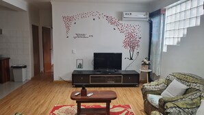 En stue med et fladskærms-TV på et sort stativ, et træsofabord, en sofa med blomstermønster og en måtte med røde og hvide mønstre.