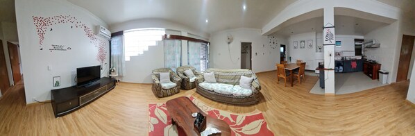 Amplia sala de estar con televisor de pantalla plana, dos sofás estampados, una mesa de centro de madera y un comedor con sillas y una mesa.