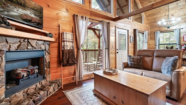 A cozy cabin interior with a stone fireplace, wooden furniture, and large windows. - Dog Friendly Cabin - Close to Gatlinburg - Fire pit - Outdoor Movie Projector (Sevierville)