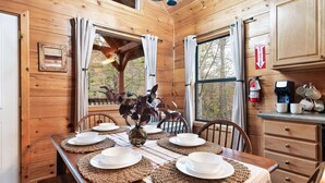 A wooden cabin interior with a dining table set for four, a fire extinguisher, and a view of trees through the windows. - Dog Friendly Cabin - Close to Gatlinburg - Fire pit - Outdoor Movie Projector (Sevierville)