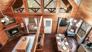 A cabin with a stone fireplace, wooden dining table, and a cozy seating area. - Dog Friendly Cabin - Close to Gatlinburg - Fire pit - Outdoor Movie Projector (Sevierville)