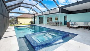 A swimming pool with a glass enclosure, a patio area with outdoor furniture, and a view of a house in the background. - Casa Azul - 3 Bedroom + Den 2 Bath Coastal Flair (Cape Coral)