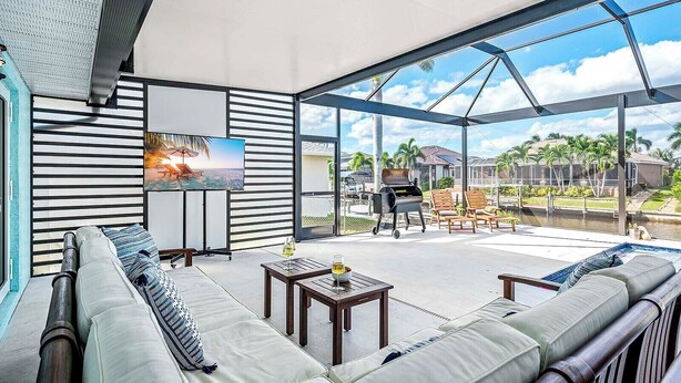 A spacious outdoor area with a modern design, featuring a large seating area with a sofa and chairs, a grill, and a TV mounted on a wall. - Casa Azul - 3 Bedroom + Den 2 Bath Coastal Flair (Cape Coral)