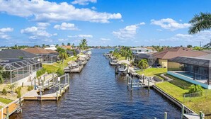 A canal with boats docked on both sides, surrounded by residential buildings and greenery. - Casa Azul - 3 Bedroom + Den 2 Bath Coastal Flair (Cape Coral)