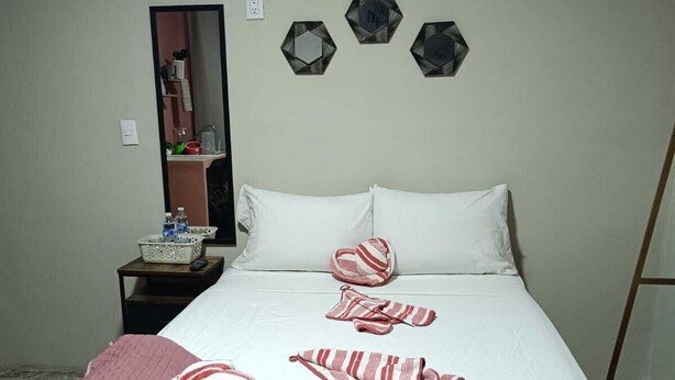 A neatly made bed with a white and pink striped blanket, a red throw pillow, and matching striped towels on the bed. There are three hexagonal wall decorations above the bed. - Loft 103 Córdoba Downtown Parking (Córdoba)