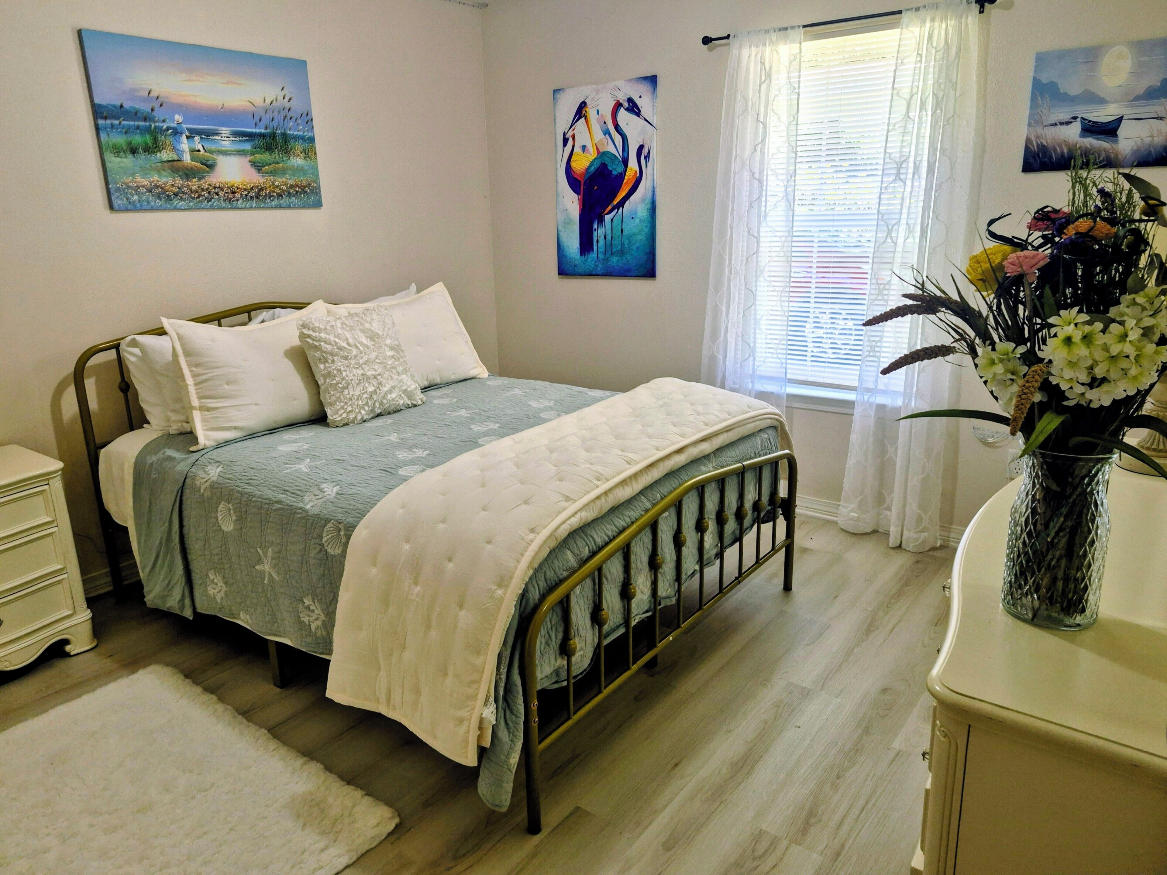 A bedroom with a bed, bedside tables, a dresser, a window with curtains, and wall art.
