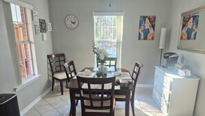 A dining area with a table set for four, surrounded by chairs, a clock, and artwork on the walls.