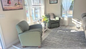 A living room with a patterned armchair, a sofa, a small table with a plant, and a rug.