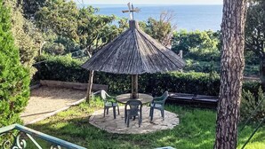 A gazebo with a windmill, surrounded by greenery and a view of the sea.