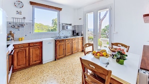 A kitchen with wooden cabinets, a white dishwasher, a microwave, and a window overlooking greenery.