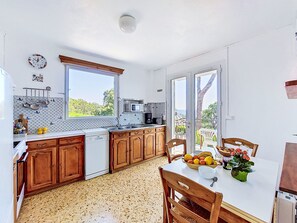 Cozinha com armários de madeira, lava-louças branca, micro-ondas e janela com vista para o verde.