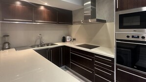 Eine moderne Küche mit dunklen Holzschränken, einer weißen Arbeitsplatte und Edelstahlgeräten, inklusive eingebautem Backofen.