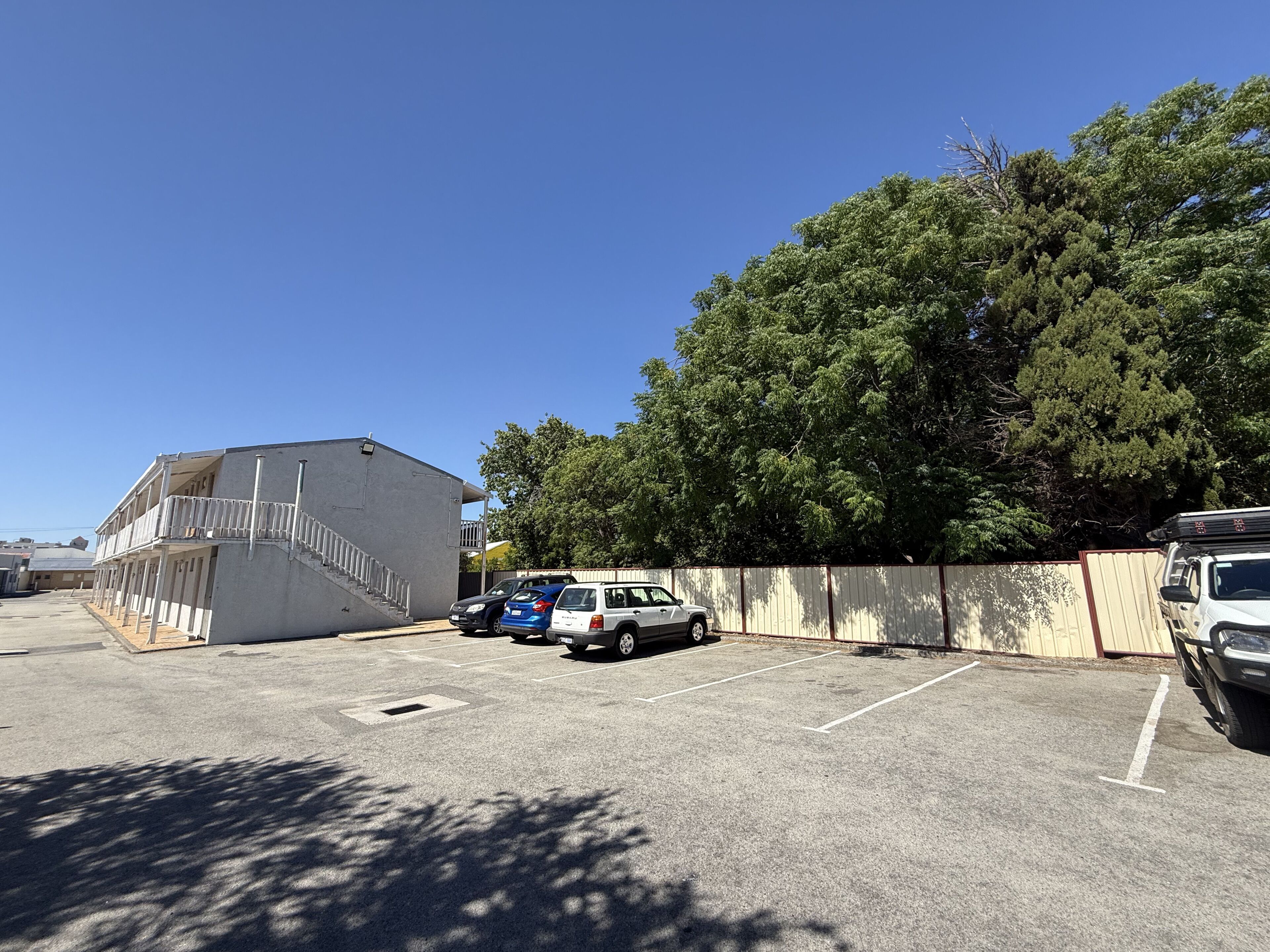 A parking lot with several cars, a building with a balcony, and a large tree.