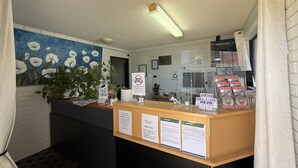 A reception desk with a blue floral painting, a plant, and informational signs including a 'Zero Tolerance' policy. - Budget Motel Midland (Midland)
