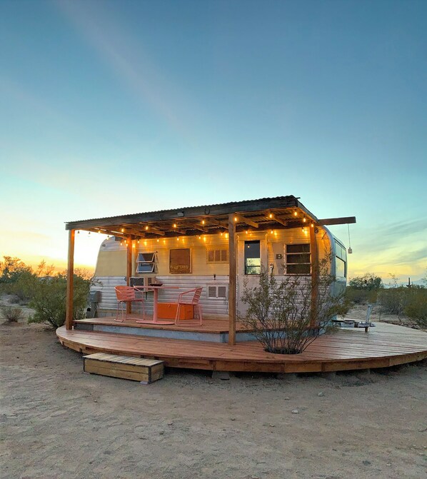 Une maison mobile dotée d’un patio couvert, d’un espace salon extérieur et d’un petit jardin.