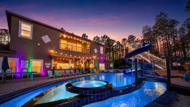 Un área de piscina con jacuzzi, tobogán y zona de bar con asientos al aire libre.