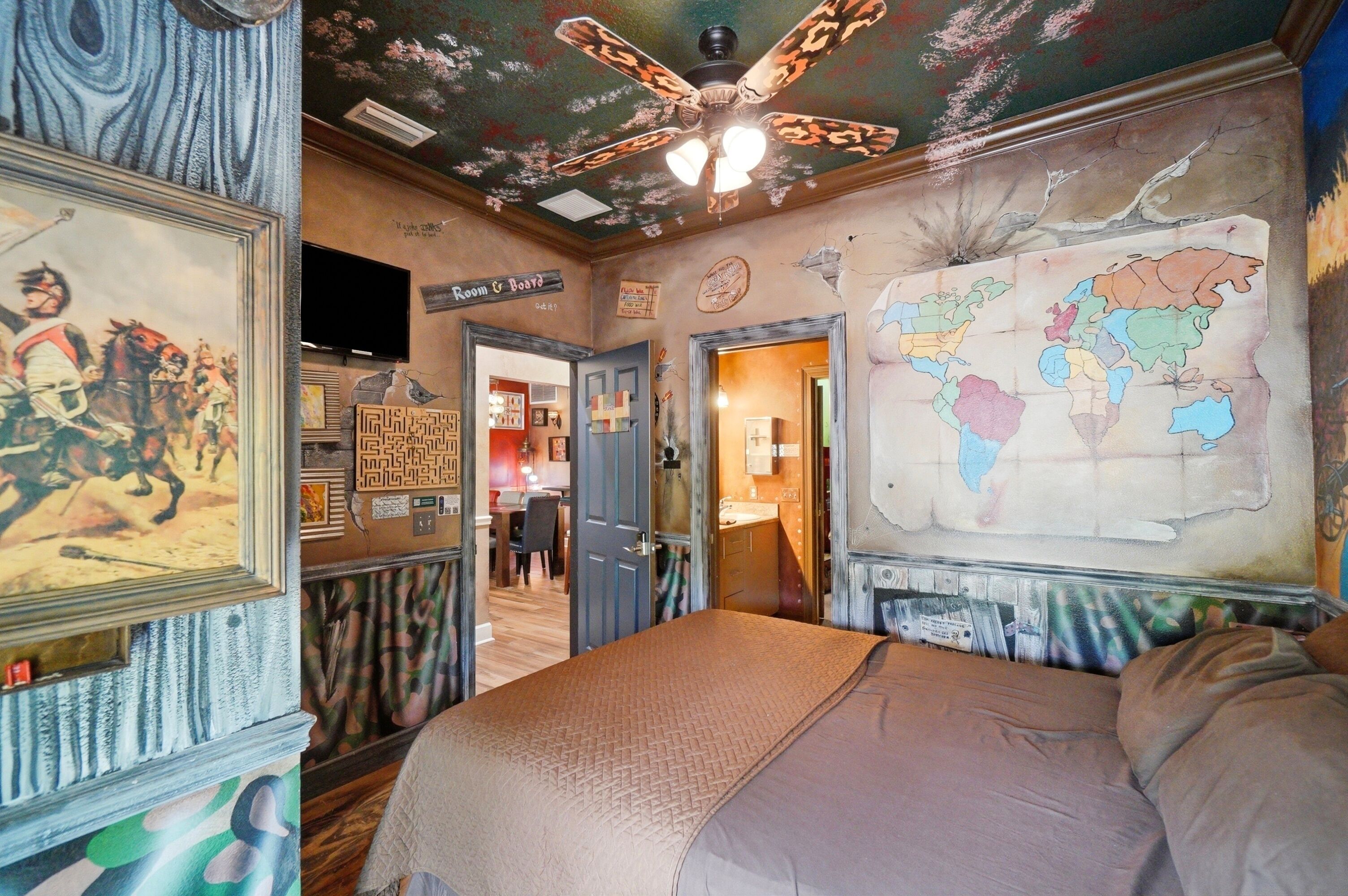 Una habitación con cama, ventilador de techo, un mapa en la pared y una puerta que da a otra habitación.