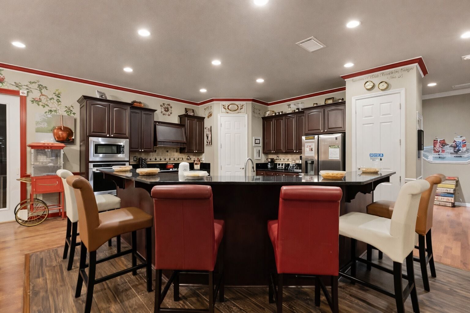 Une cuisine moderne avec un îlot central, des meubles en bois foncé et des tabourets de bar rouges.