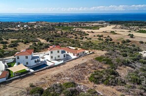 Une propriété située sur la côte, avec un bâtiment blanc doté d’un toit recouvert de tuiles rouges, une piscine et une vue sur la mer.