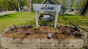 A welcome sign with a farm logo and a small building in the background. - Hidden Oaks | Lodge Cabin | Unit 3 (Birch Run Township)