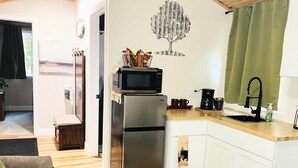 A compact kitchen with a refrigerator, microwave, and coffee maker. A dining area with a table and chairs is visible. - Hidden Oaks | Lodge Cabin | Unit 3 (Birch Run Township)