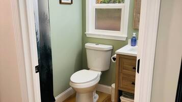 Une petite salle de bain avec des toilettes, une fenêtre donnant sur des arbres et un meuble en bois contenant des serviettes.