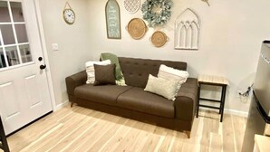 A living room with a brown sofa, a small side table, a wall clock, decorative wall art, and a door.