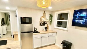 A modern kitchen with a stainless steel refrigerator, a coffee-themed wall decoration, and a TV mounted on the wall.