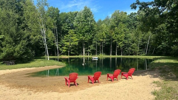 A sandy beach area with red chairs and a lake surrounded by trees.