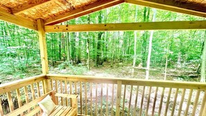 A wooden deck with a bench, surrounded by a forest.