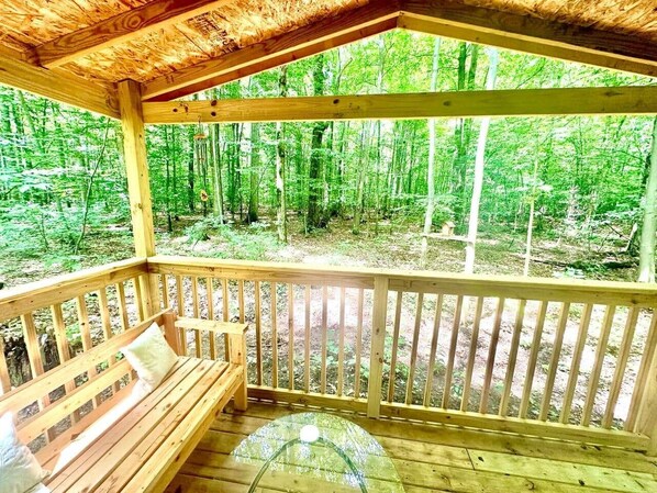 Una terraza de madera con un banco, rodeada de un bosque.