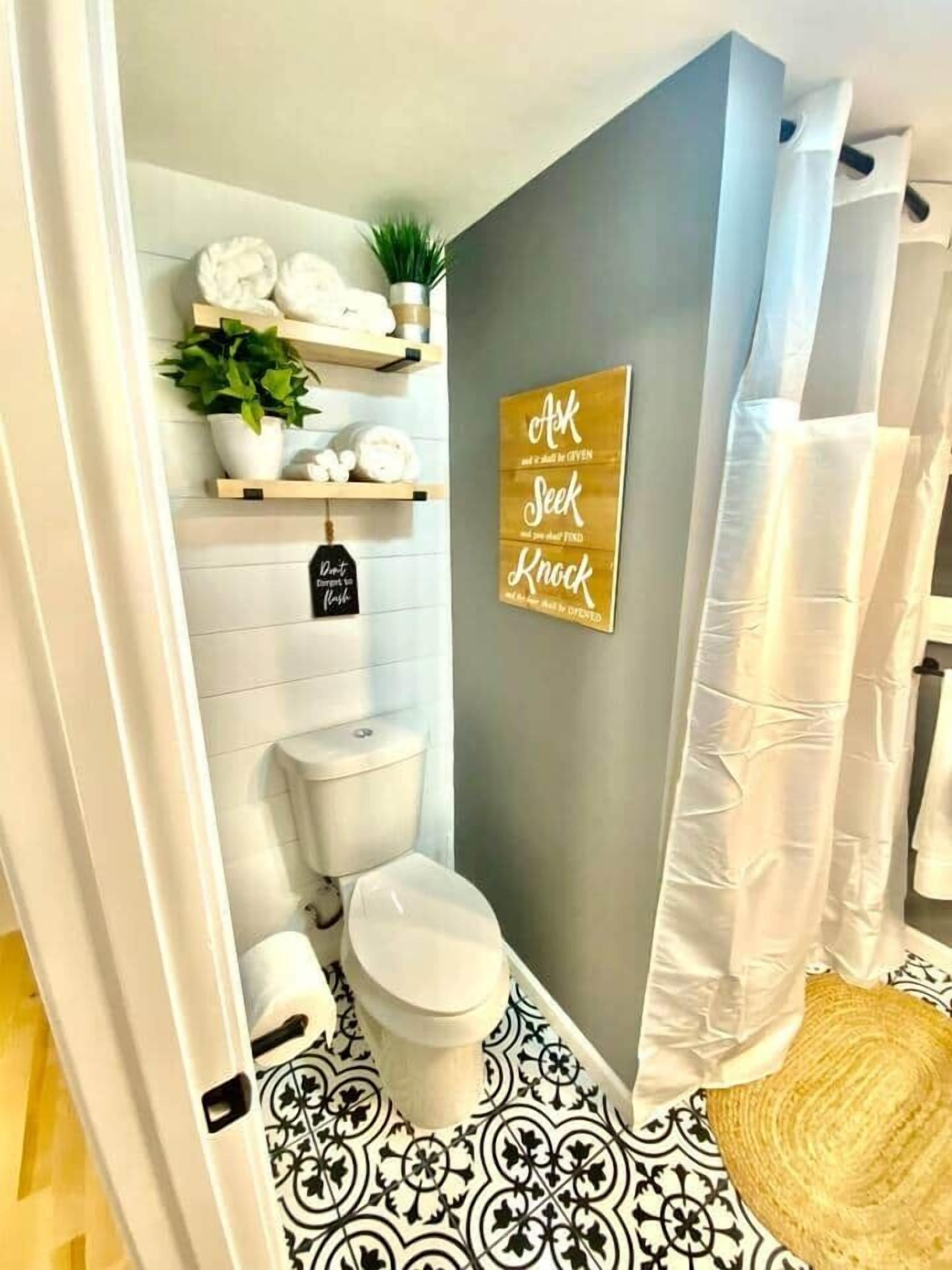 Un baño con inodoro, cortina de ducha, toallero y un cartel en la pared.