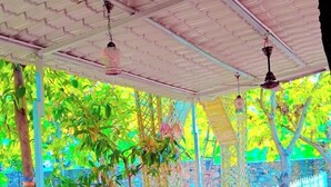 Un espace extérieur aménagé avec des chaises et une table en osier, entouré d’une clôture en bambou et de verdure.