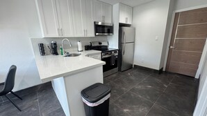 Una cocina moderna con armarios blancos, electrodomésticos de acero inoxidable y un cubo de basura negro.