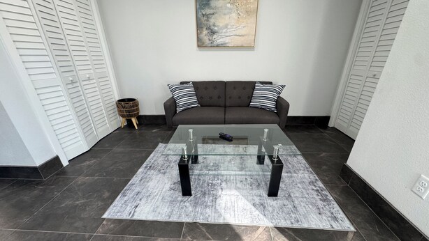 Un salón moderno con una mesa de centro de vidrio, un sofá oscuro y un cuadro en la pared.