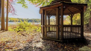Ein hölzerner Pavillon mit Glasveranda, umgeben von Herbstlaub und Blick auf einen See.
