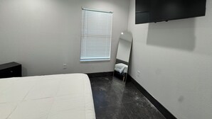 Une chambre à coucher avec un lit, un téléviseur fixé au mur, une fenêtre avec des stores et un miroir.