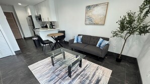 Un salon moderne avec une table basse en verre, un canapé gris et un coin repas comprenant une table ronde et des chaises.