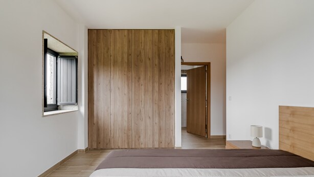 A bedroom with a wooden wardrobe, a bed with patterned bedding, a bedside table with a lamp, and a window with a view of the outside. - Casa do Tojal - A refuge in the Minho mountains (Igreja)