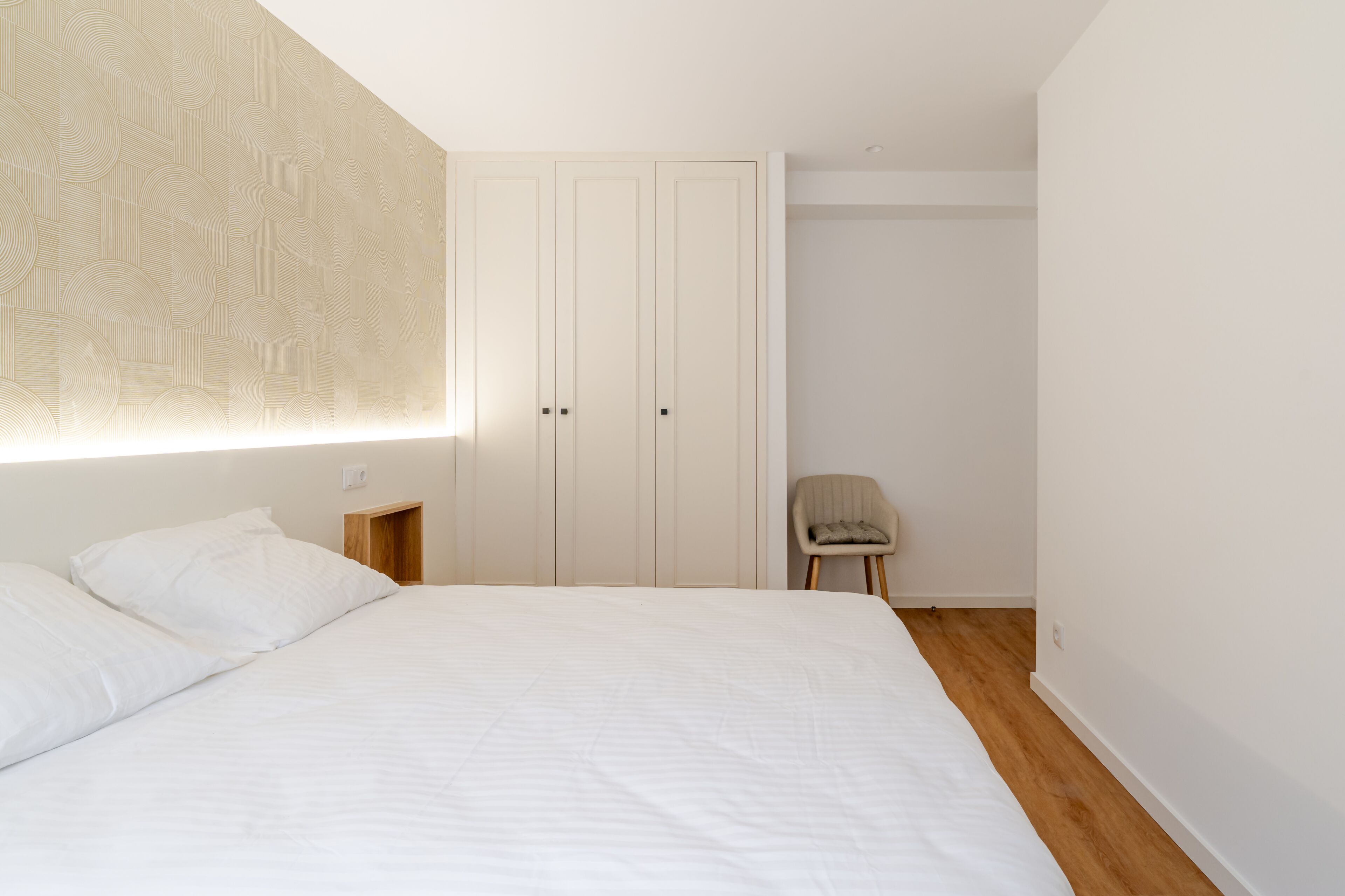Ein Schlafzimmer mit einem großen Bett, einem Kleiderschrank, einem Sessel und einer Wand mit Muster.